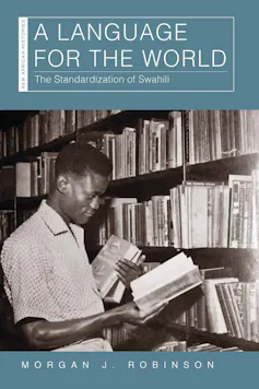 A book cover with a black and white photo of a man in a library, holding some books in one hand and reading from a book in the other.