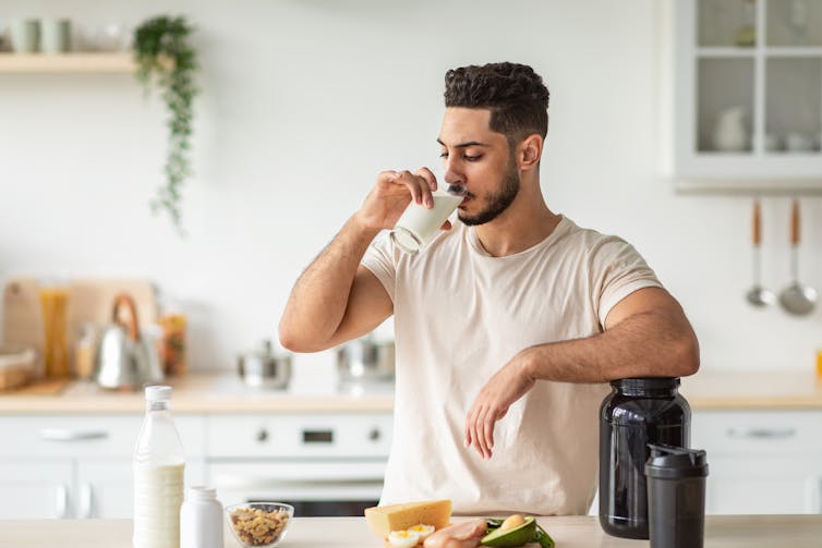 Un uomo beve un bicchiere di latte o un frullato proteico nella sua cucina.