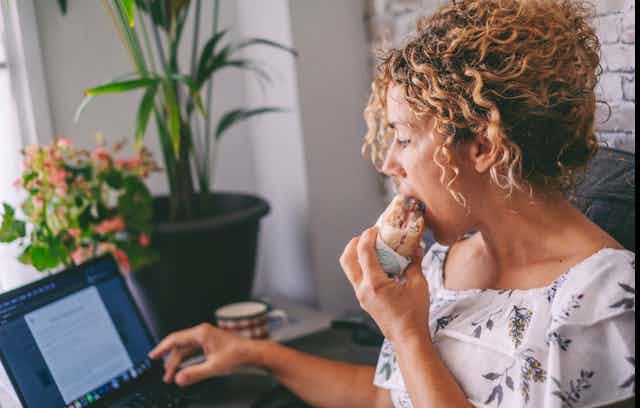 Mujer comiendo un bocadillo mientras trabaja en el ordenador.