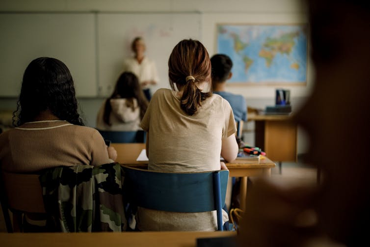 View of a classroom, with the educator teaching while standing next to a map of the world.