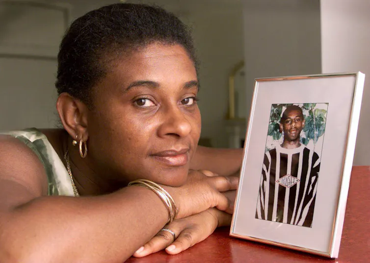Photo of Doreen Lawrence, resting her head on her hands, next to a framed photo of her son Stephen