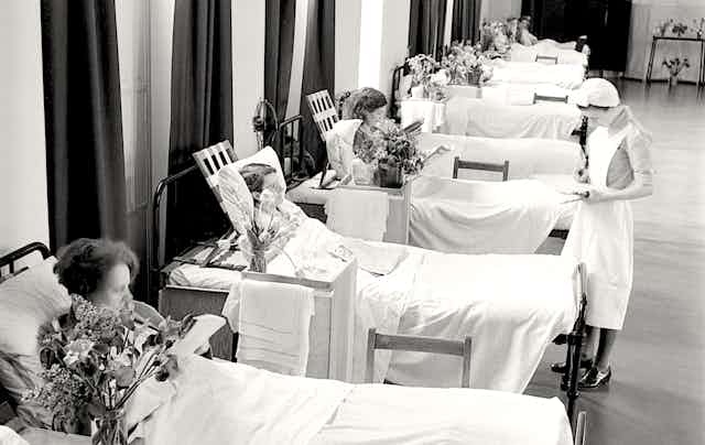 A nurse inspects patients in a row of hospital beds