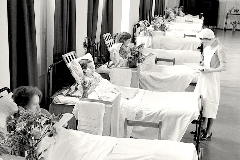 A nurse inspects patients in a row of hospital beds