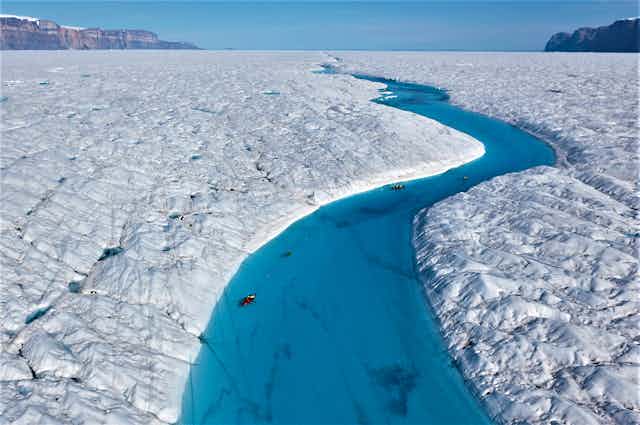 An ice blue river of meltwater weaves over the cracked surface of a Greenland glacier.