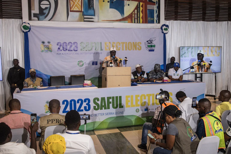 A man standing in front of a big banner while addressing a group of people.