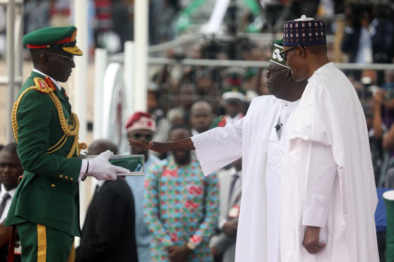 Two men in white native attire facing a man in full ceremonial military uniform.