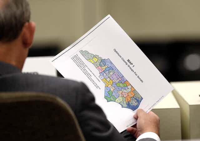 A person, seen from behind, holds a map of North Carolina with voting districts marked in different colors.