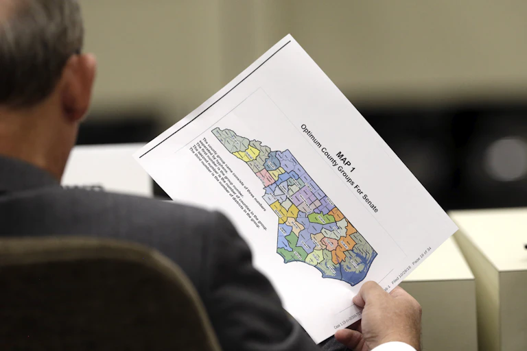 A person, seen from behind, holds a map of North Carolina with voting districts marked in different colors.