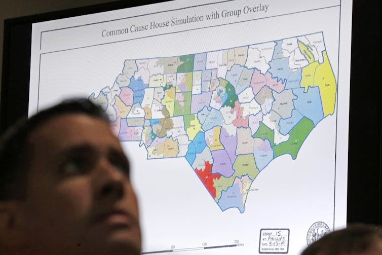 Una persona se para frente a un gran mapa que muestra los distritos electorales de Carolina del Norte.
