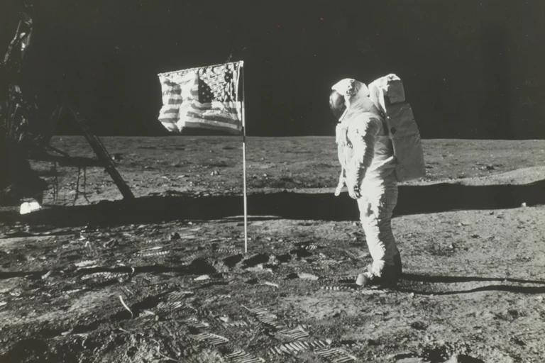 Standing on the Moon's dusty surface, an astronaut pauses to look at the U.S. flag.
