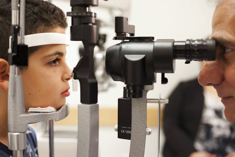 Child looking into a slip lamp microscope for an eye exam with a doctor