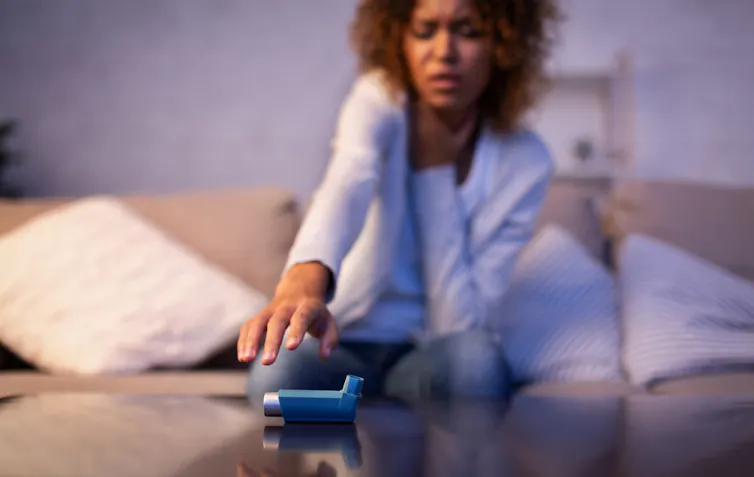 Woman clutching throat reaching for asthma inhaler on table