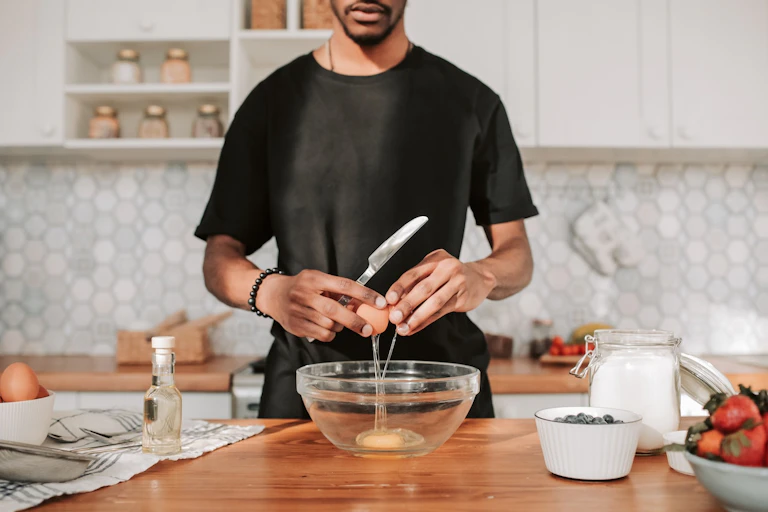Man breaking egg into mixing bowl in kitchen counter