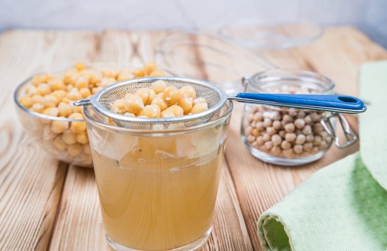 Chickpeas in strainer sitting over glass of aquafaba