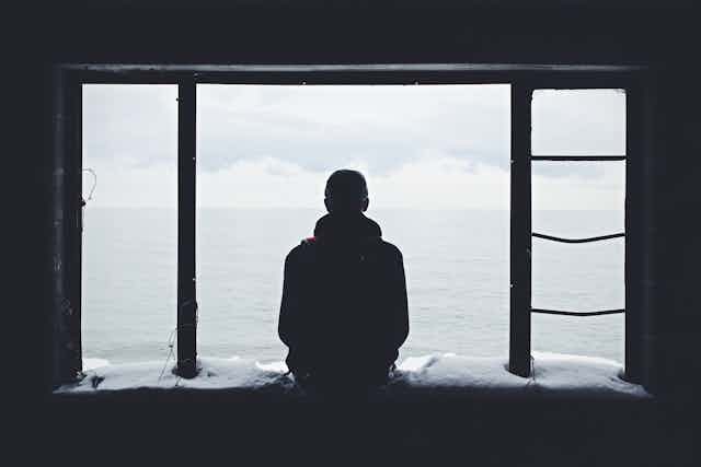 Silhouette of a person sitting on a snowy windowsill