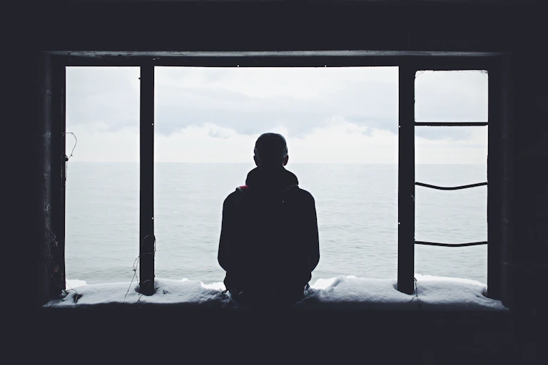 Silhouette of a person sitting on a snowy windowsill