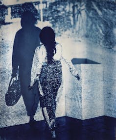 A woman walking towards a wall-sized photograph of a woman's shadow.