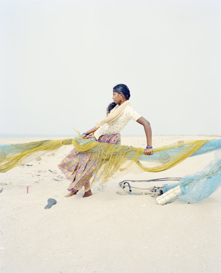 An Indian woman pulling a fishing net up a beach in the wind.