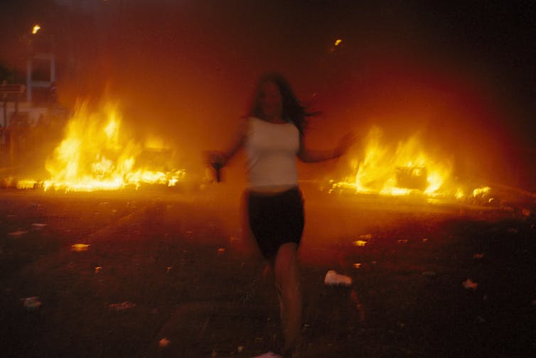The silhouette of a girl running from leaping flames towards the camera.
