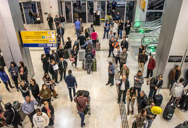 Overhead shot of travellers and others walking around and waiting in an airport arrivals hall