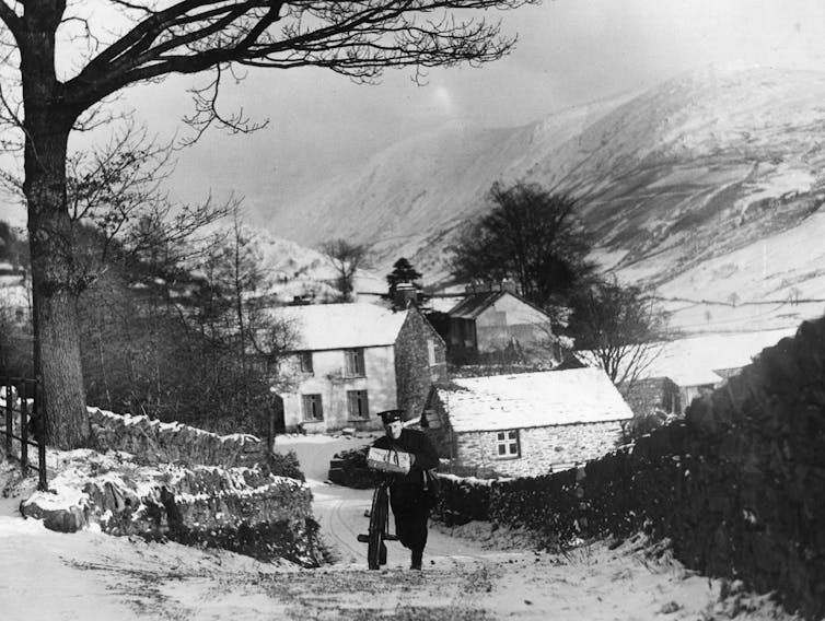 1938 black and white photo of postman pushing bike up hill in village