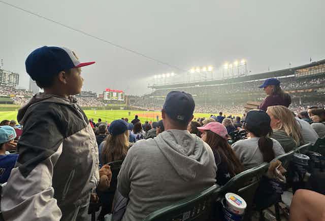 A young boy stands up among fans watching the Phillies-Cubs game. Smoke is evident in the air.