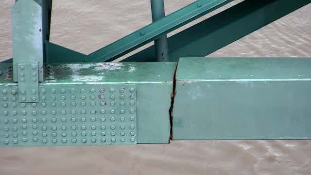 A green steel girder with a crack through it and the two halves slightly displaced