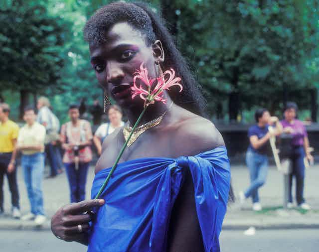 A Black man is wearing lipstick and holding a flower. 