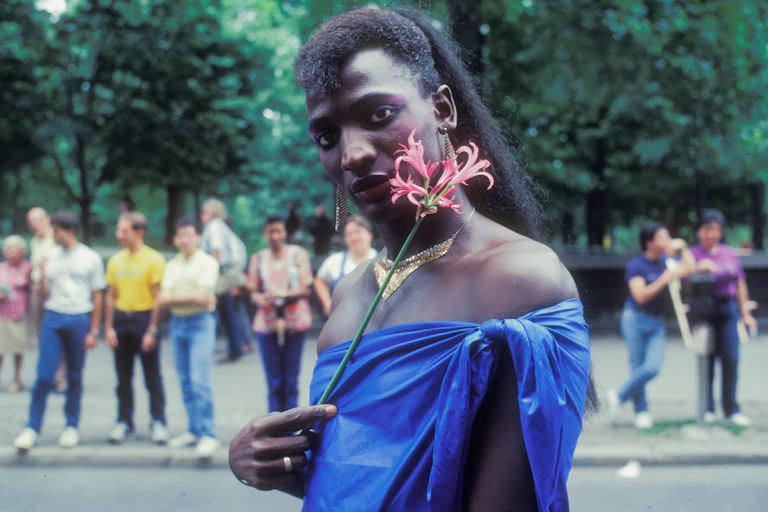 A Black man is wearing lipstick and holding a flower.