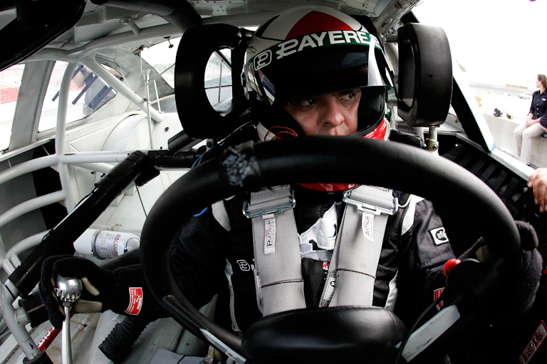 Driver wearing helmet, gloves and a suit behind the wheel.