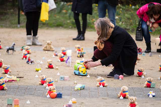 A woman kneels down in front of a small toy, lined up with rows of other toys on the ground. 