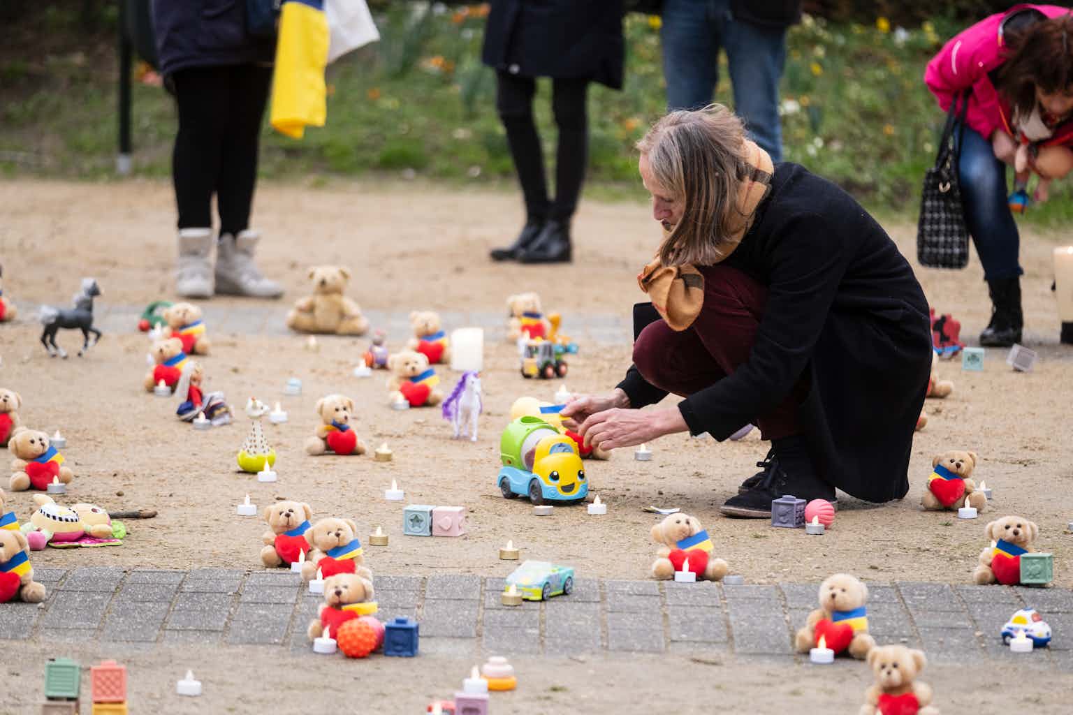 A woman kneels down in front of a small toy, lined up with rows of other toys on the ground.