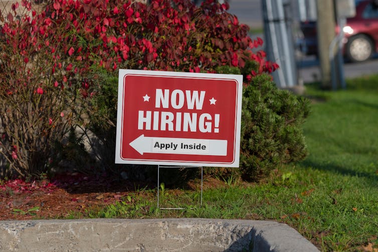 A 'Now Hiring' sign posted on a lawn