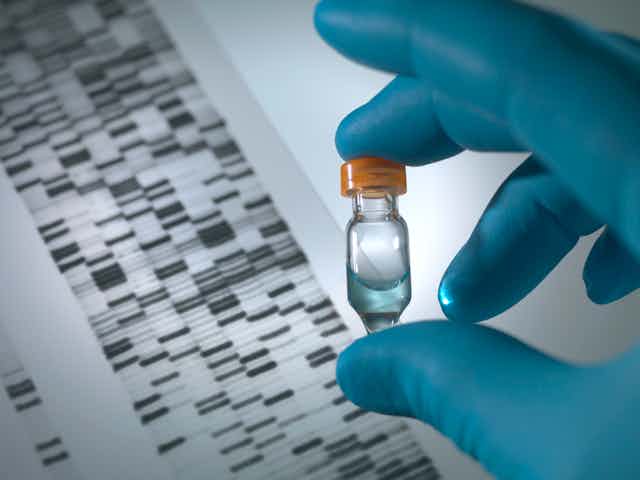 Gloved hand holding DNA sample vial over a DNA autoradiogram