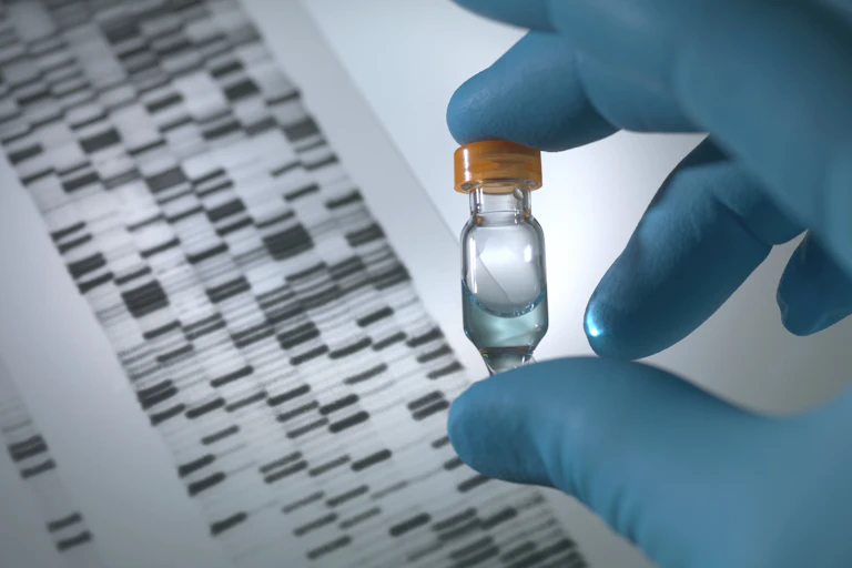Gloved hand holding DNA sample vial over a DNA autoradiogram