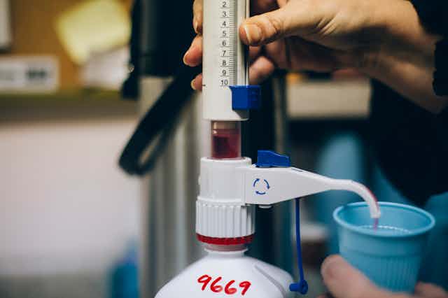 Photo of a hand dispensing a measured dose of red liquid.