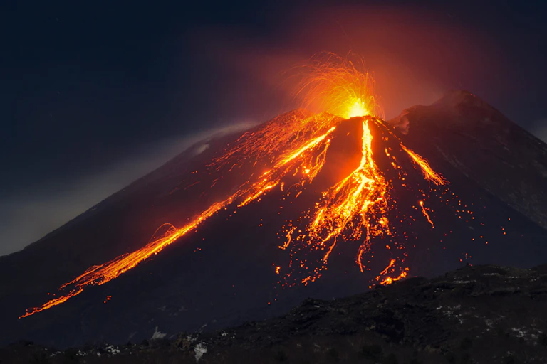A dark mountain with orange glowing lava at night