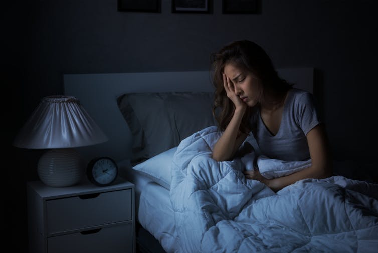 Young woman sitting in bed, hand in face, in the dark