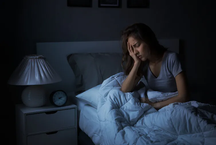 Young woman sitting in bed, hand in face, in the dark
