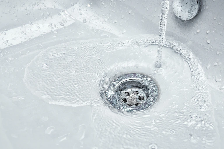 Water pours down a white sink basin into the silver drain
