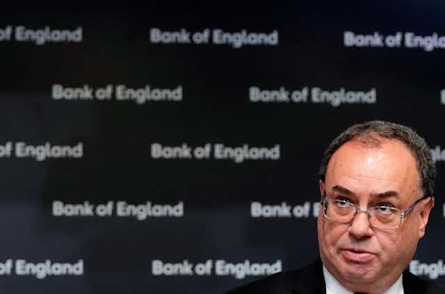 Image of man in glasses in front of background that says "Bank of England" in a repeated pattern