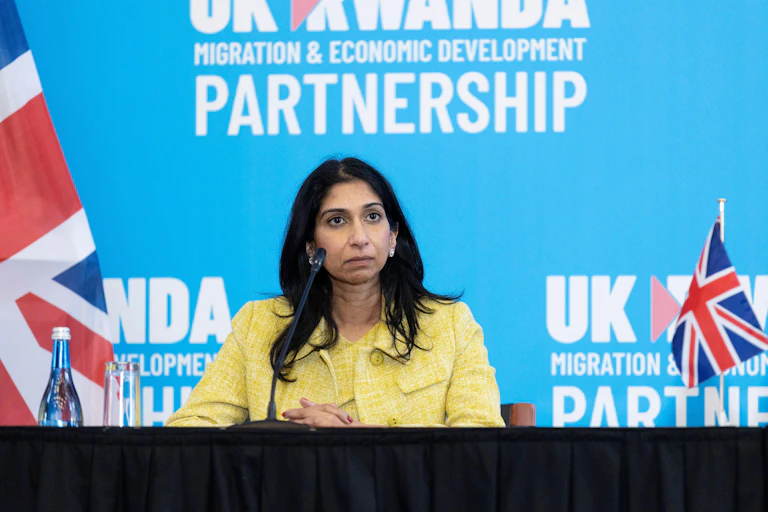 Suella Braverman sitting at a table in front of a blue wall that reads UK Rwanda migration and economic development partnership
