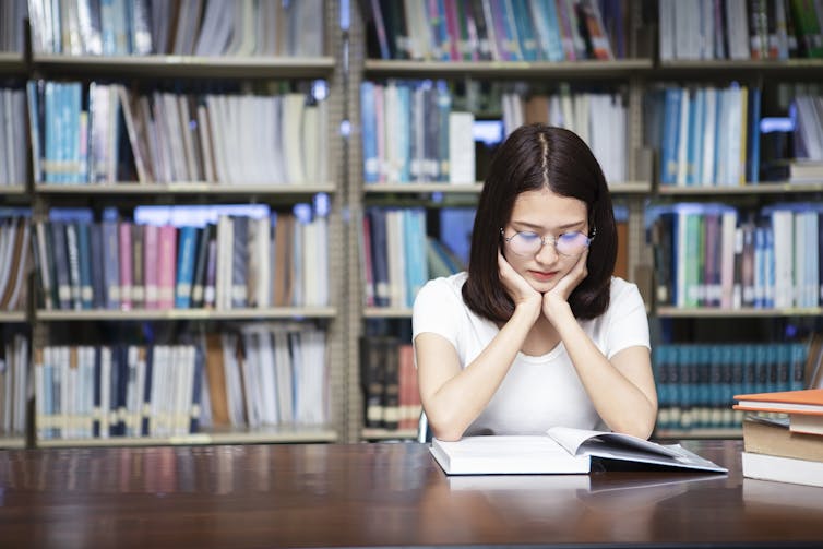 Student reads textbook in library.