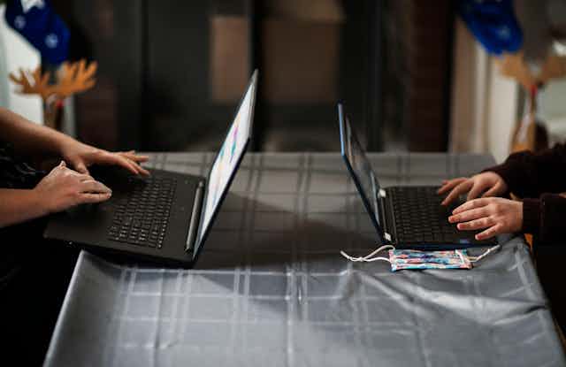 The arms of two people are seen working on separate laptops on opposite sides of a table.