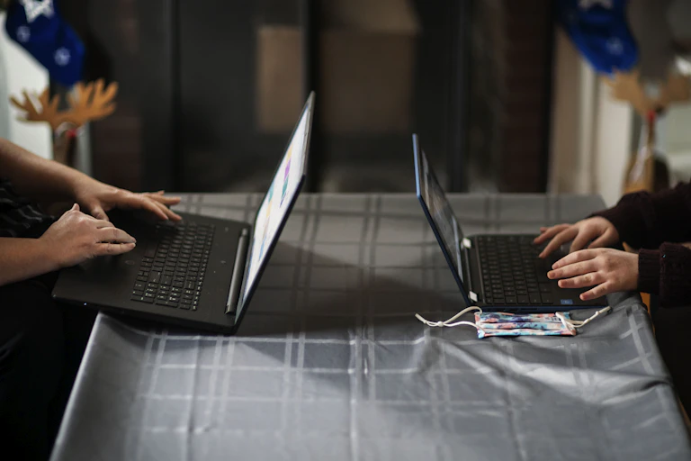The arms of two people are seen working on separate laptops on opposite sides of a table.
