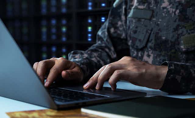 Mains d'un homme en uniforme militaire en train de taper à l'ordinateur