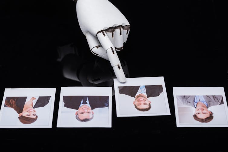 a robot hand points to one of four photographs on a shiny black surface