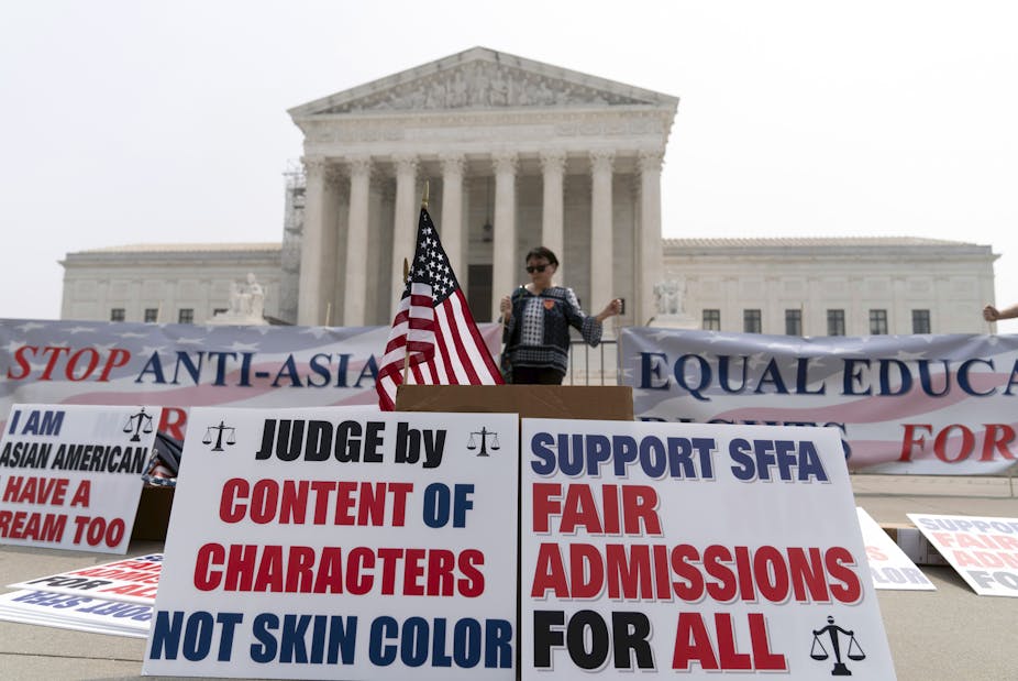A person standing outside the US Supreme Court where posters are lined up that say "judge by content of characters not skin color,' and another that says, 'Fair admissions for all.'