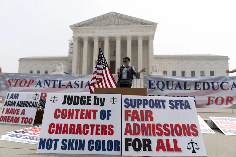 A person standing outside the US Supreme Court where posters are lined up that say "judge by content of characters not skin color,' and another that says, 'Fair admissions for all.'