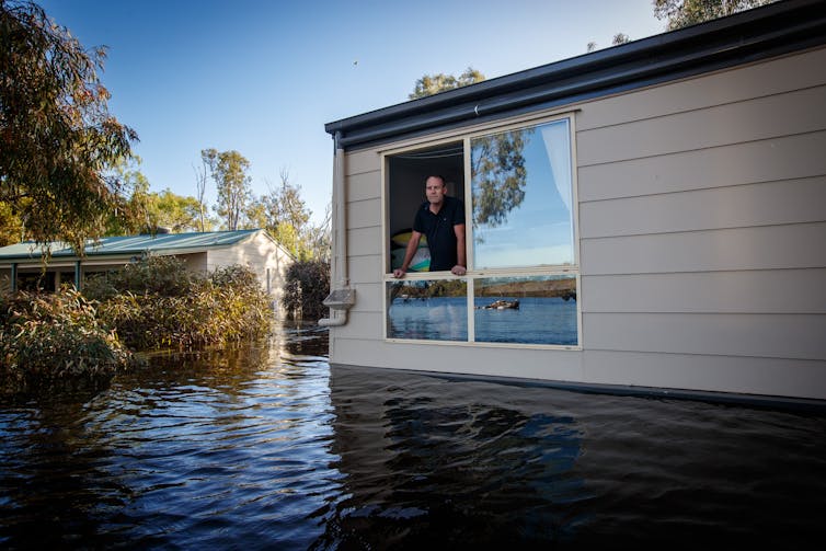 A man looks out of the second-storey window of his flooded shack at Scott’s Creek, Morgan.